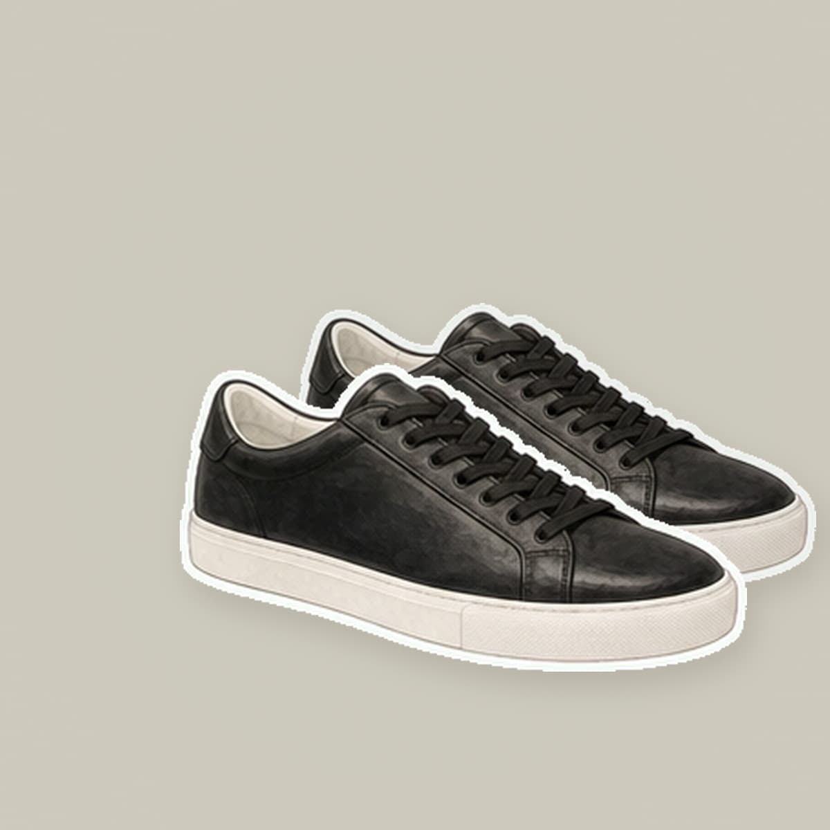 Pair of black leather low-top sneakers with white rubber midsoles on cream paper.