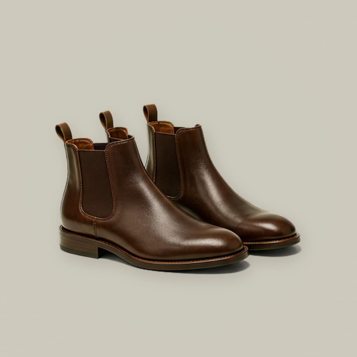 Pair of dark brown leather Chelsea boots with visible elastic gussets, on cream paper.