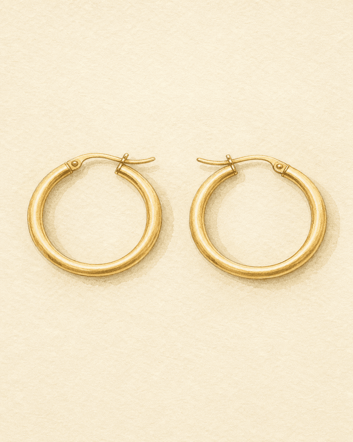 A pair of medium-scale yellow gold hoop earrings on cream paper.
