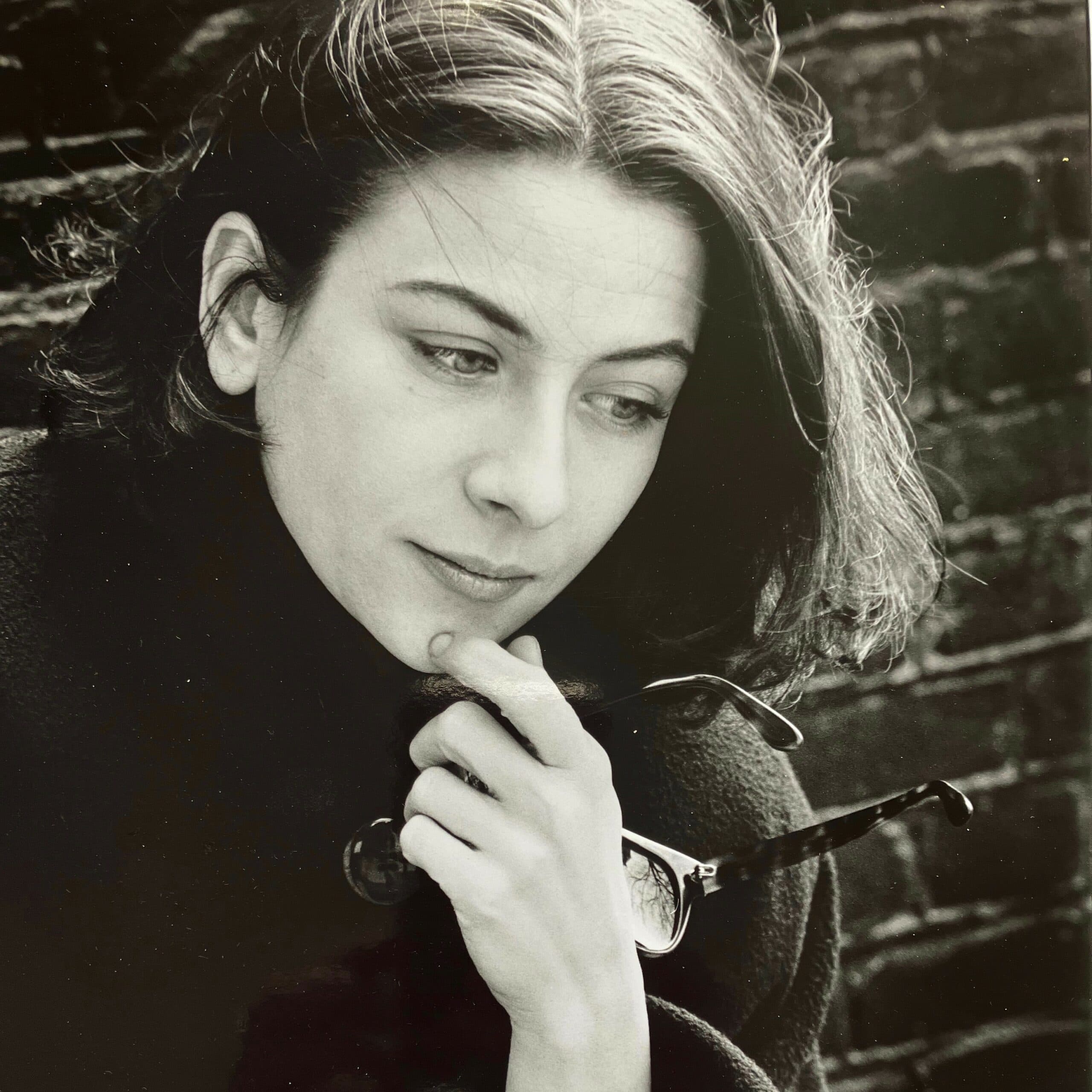 Black-and-white author portrait of Donna Tartt holding glasses.