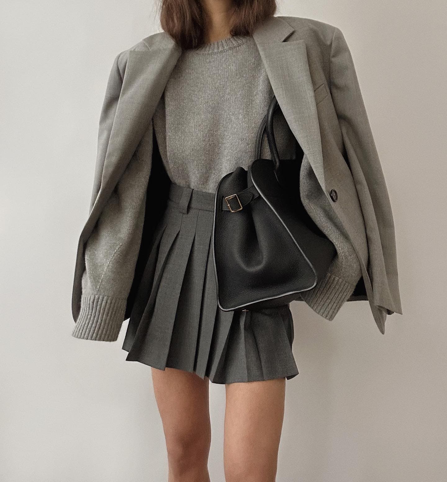 Grey pleated skirt styling reference with a dark top and loafers.